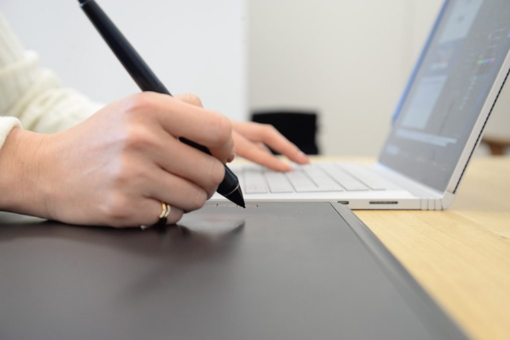 main sur un ordi et l'autre main tenant le stylo de la tablette graphique